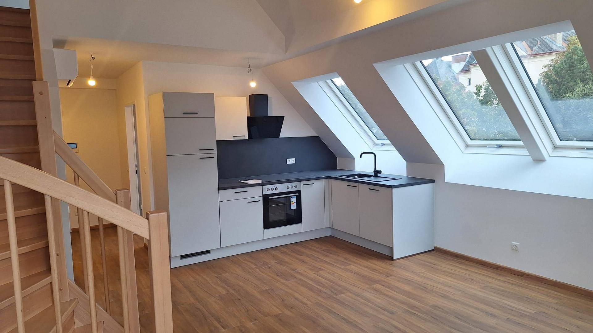 Moderne Einbauküche in Grau und Weiß mit Ofen und Spüle im hellen Dachgeschossbereich.
