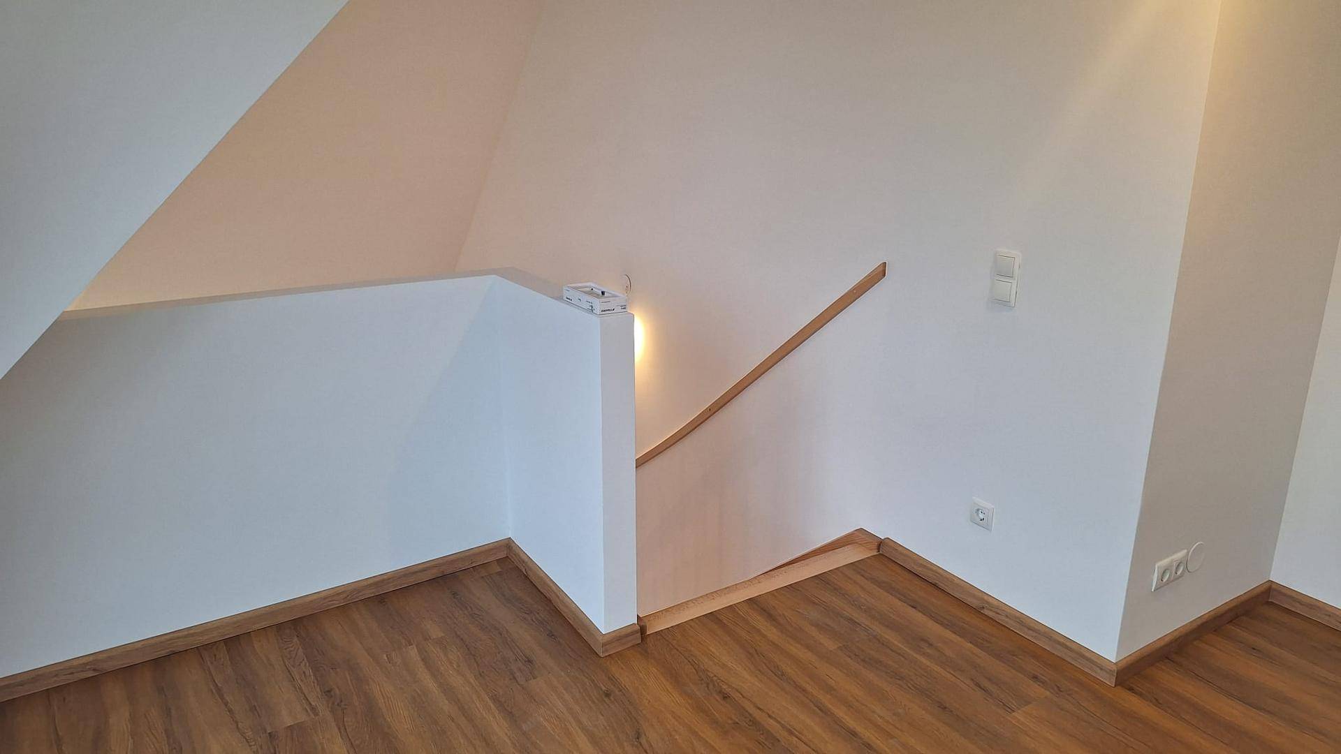Treppenbereich mit Holzgeländer und weißen Wänden, der zu einem oberen Stockwerk führt.