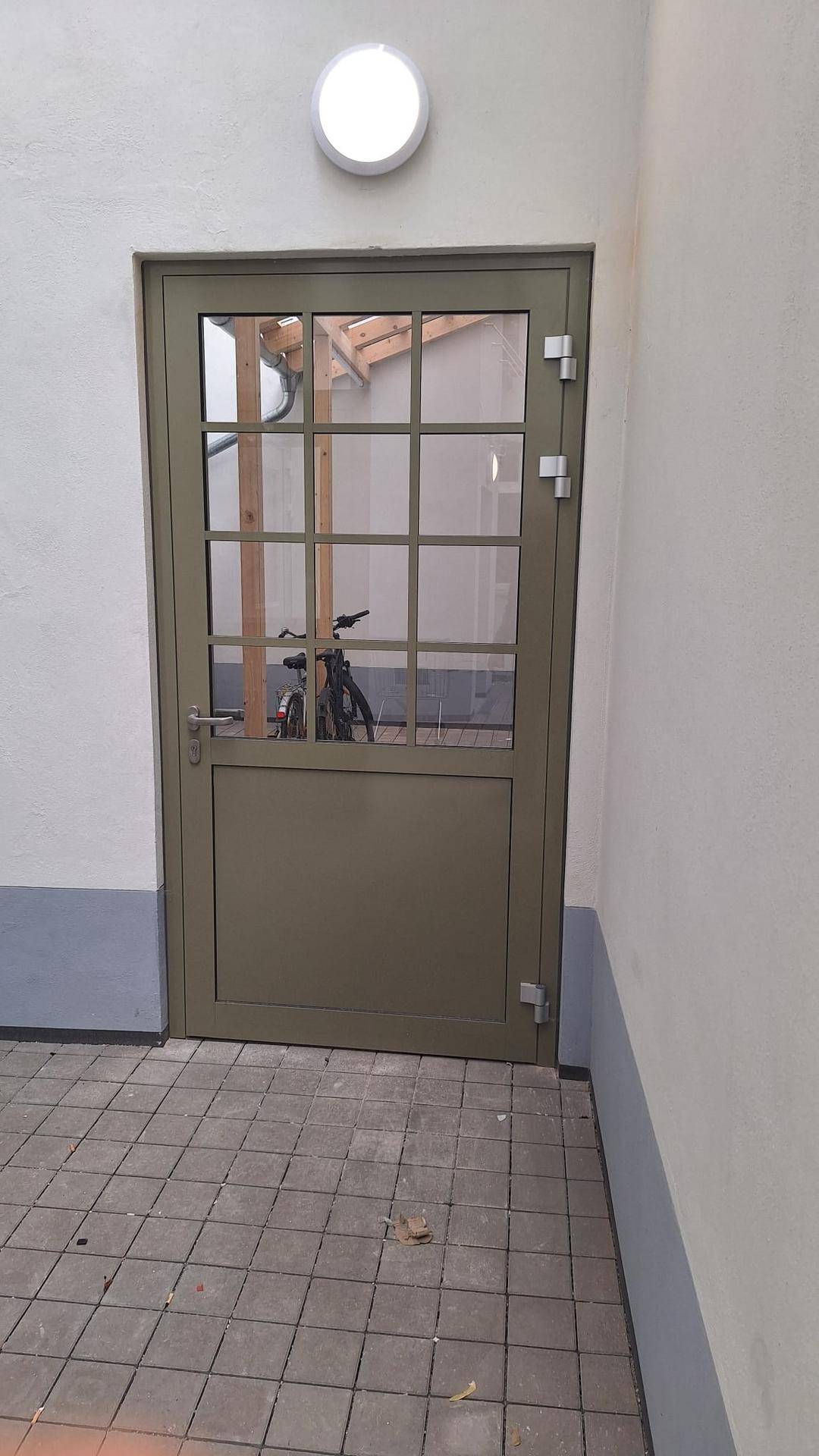 Eine moderne Glastür mit Sprossen, die zu einem Innenhof oder Fahrradraum führt.