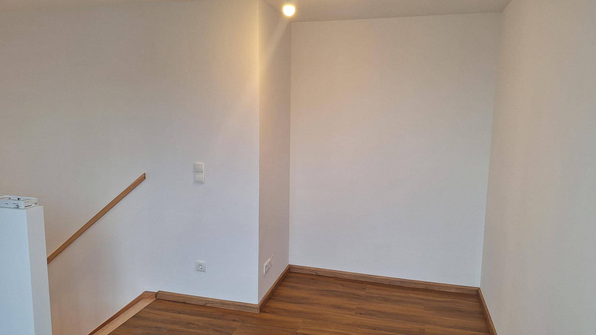 Heller Raumeck mit Laminatboden, weißen Wänden und einer Deckenleuchte.
