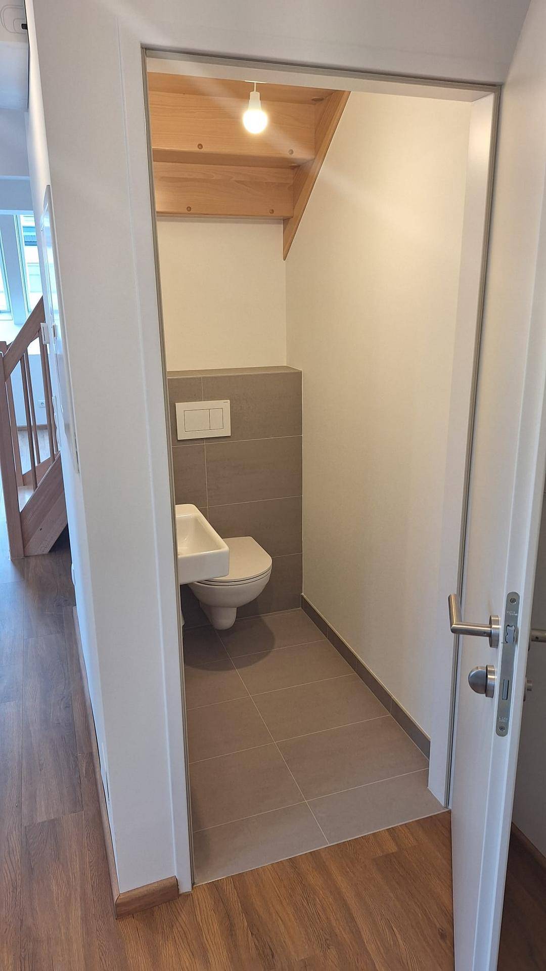 Kleines Gäste-WC mit wandhängendem WC und Waschbecken unter einer Dachschräge.