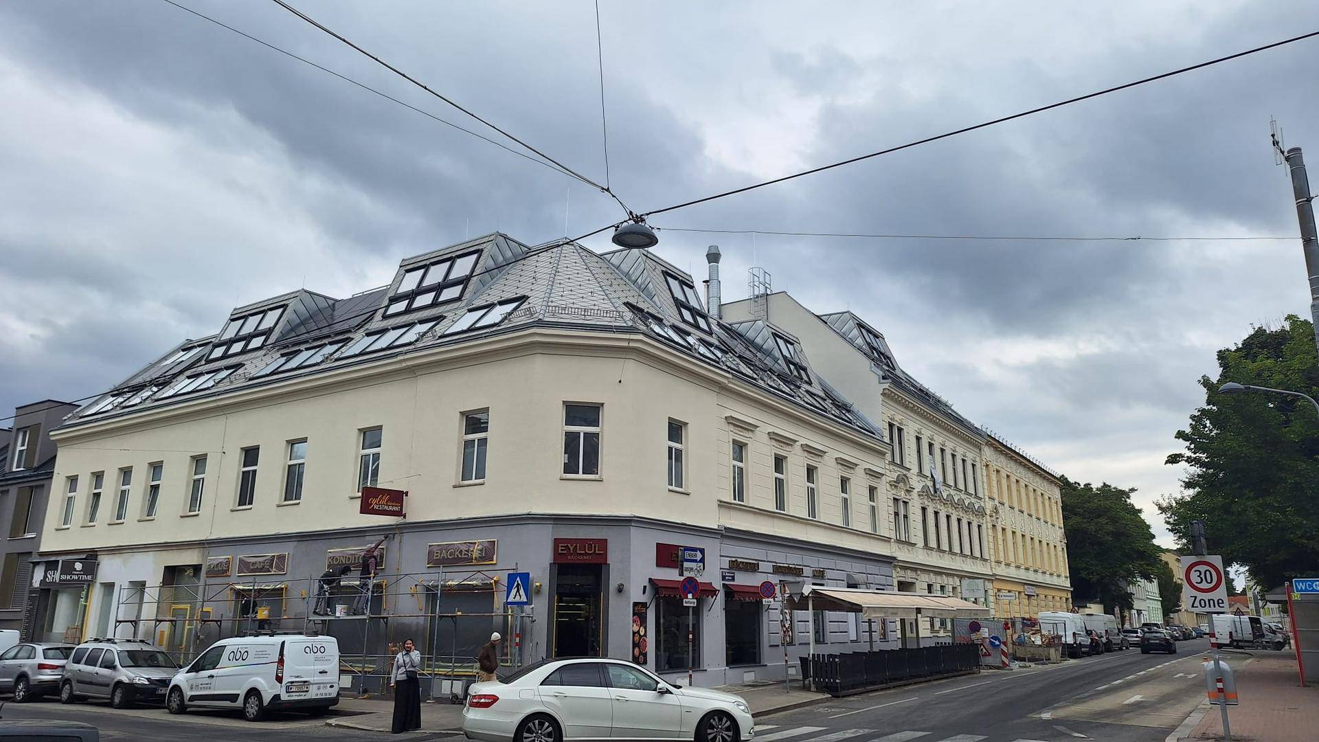 Ansicht eines Eckgebäudes mit Mansarddach und Geschäften im Erdgeschoss an einer städtischen Straße.