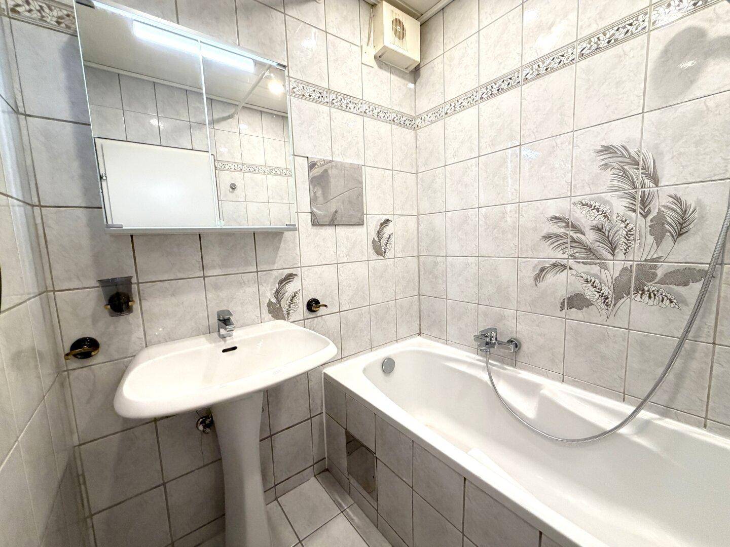 Gefliestes Badezimmer mit Badewanne, Standwaschbecken und einem Spiegelschrank, in hellem Design gehalten.