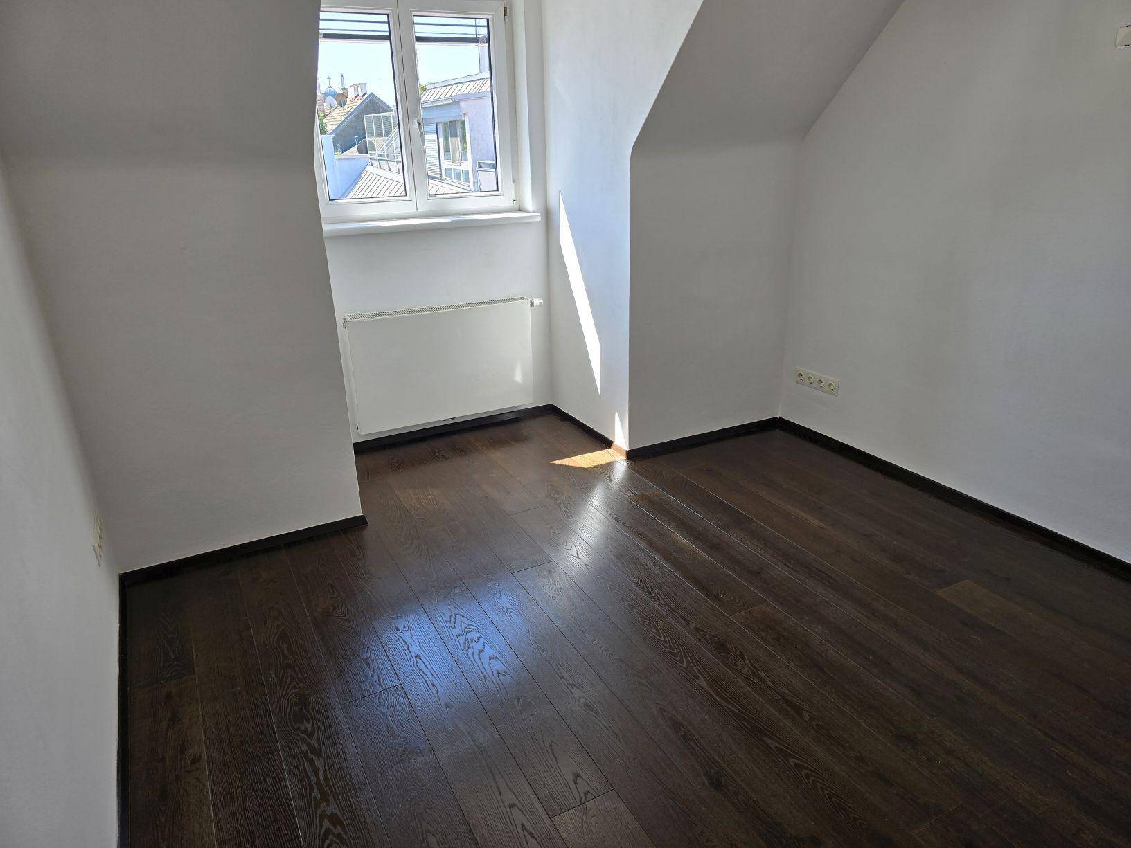 Lichtdurchflutetes Schlafzimmer mit dunklem Holzboden und schrägen Wänden im Dachgeschoss.