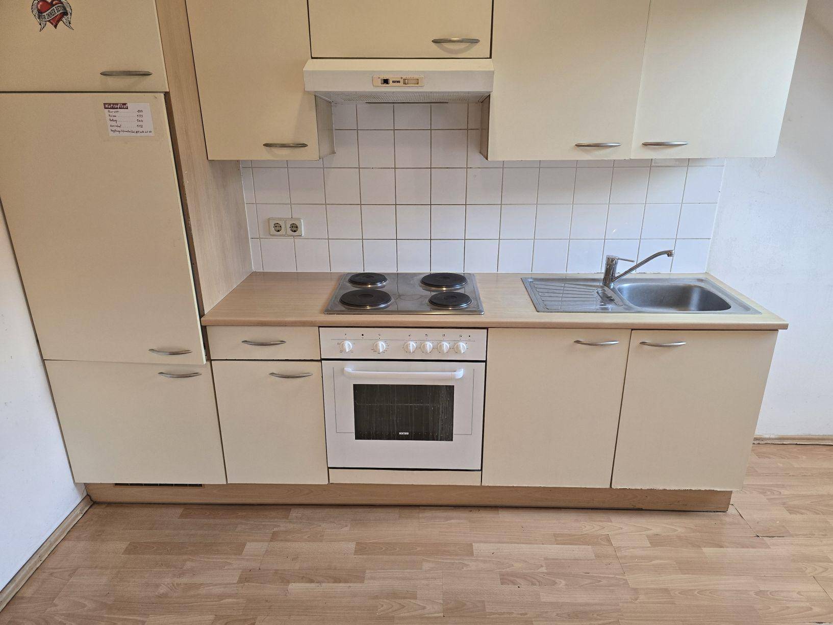 Funktionale Küchenzeile mit beigen Schränken, Elektroherd, Backofen und integriertem Kühlschrank.