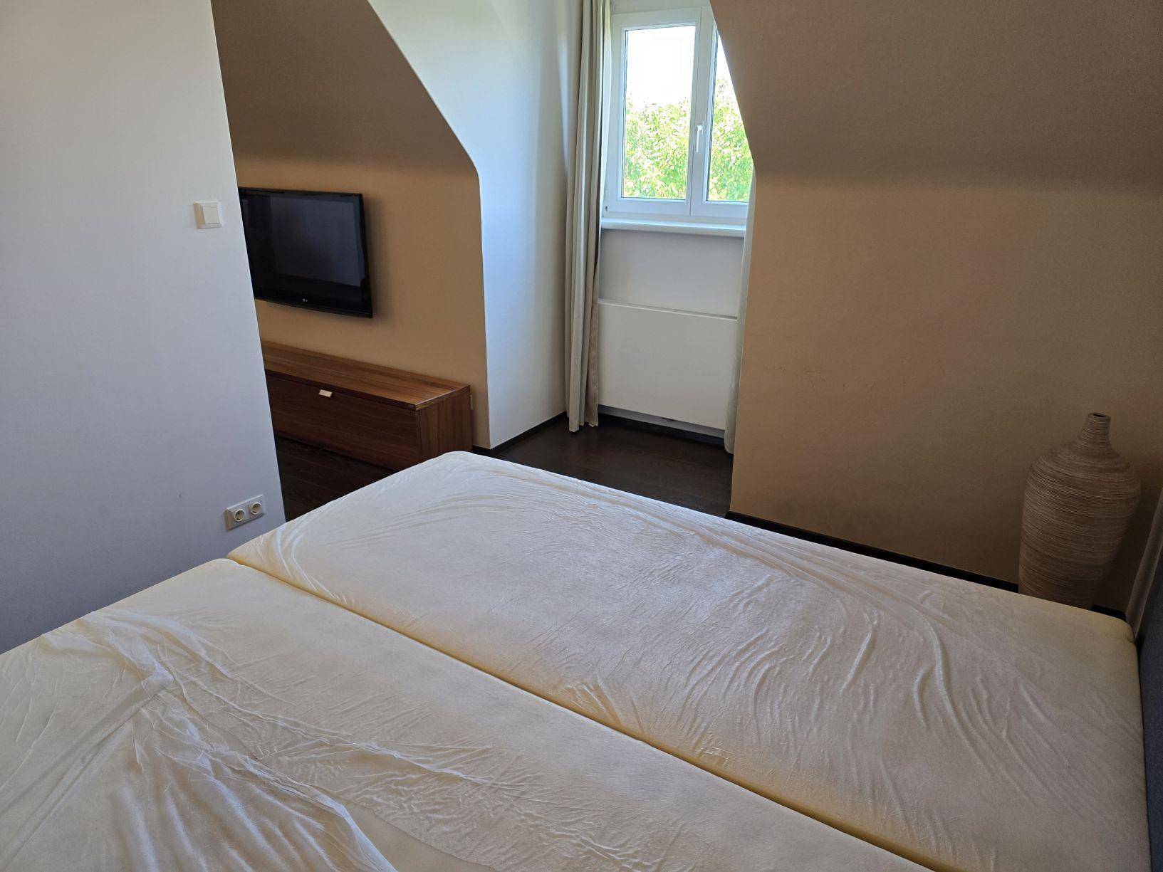 Schlafzimmer mit Doppelbett, Fenster und dunklem Holzboden, hell und freundlich.