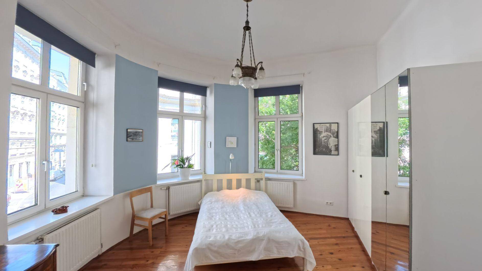 Helles Schlafzimmer mit Holzboden, blauen Wänden und großen Fenstern mit Stadtblick.