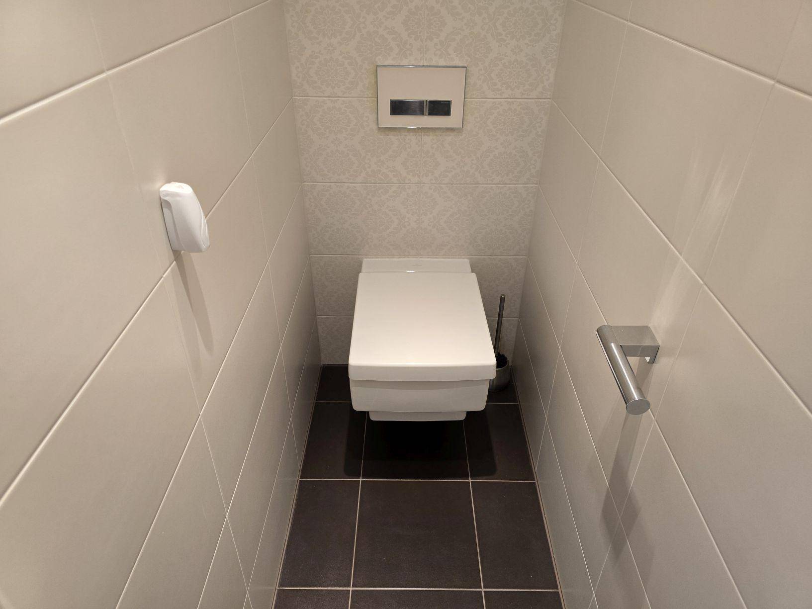 Modernes Gäste-WC mit Wand-WC, weißen Fliesen und dunklem Boden.