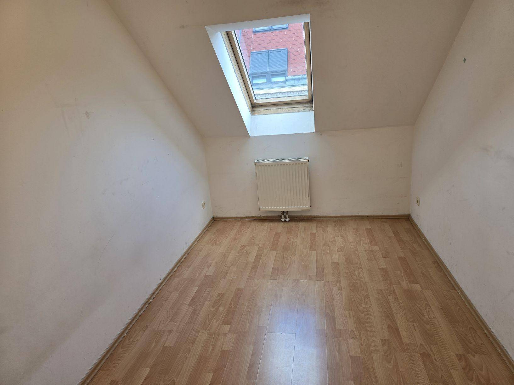 Gemütliches Dachzimmer mit Laminatboden, schräger Decke und einem Dachfenster für Helligkeit.
