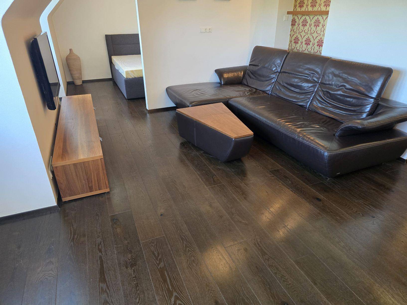 Geräumiger Wohnbereich mit dunklem Holzboden, Ledersofa und Blick auf den Schlafbereich.