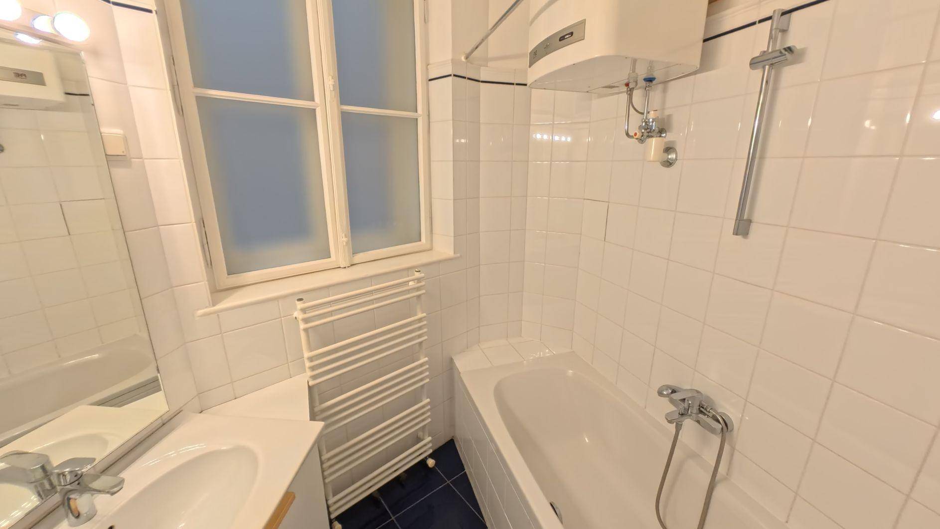 Gefliestes Badezimmer mit Badewanne, Fenster und Handtuchheizkörper in weiß-blauem Design.