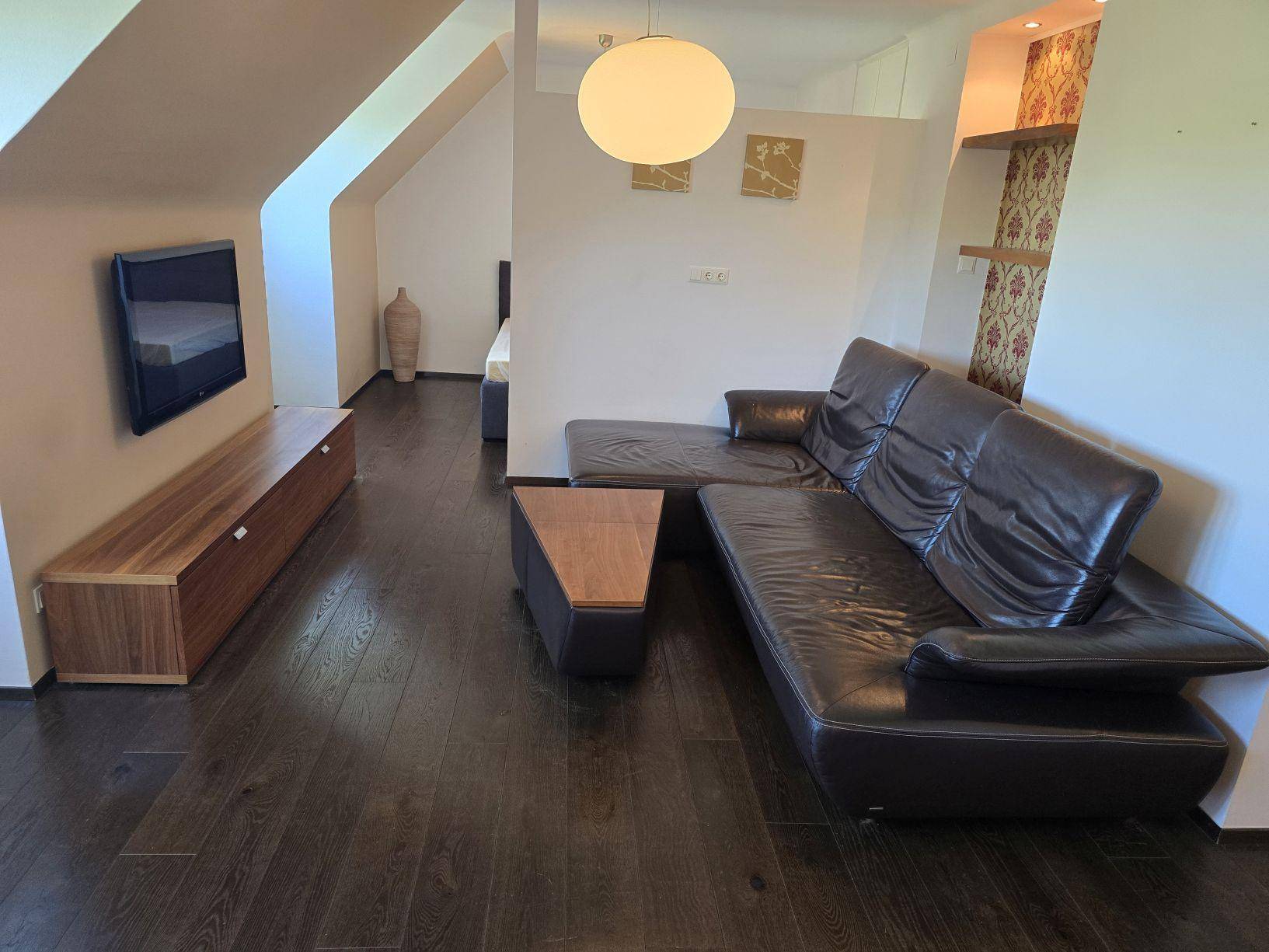 Heller Wohnbereich mit Ledersofa, Fernseher und dunklem Holzboden in offener Raumgestaltung.