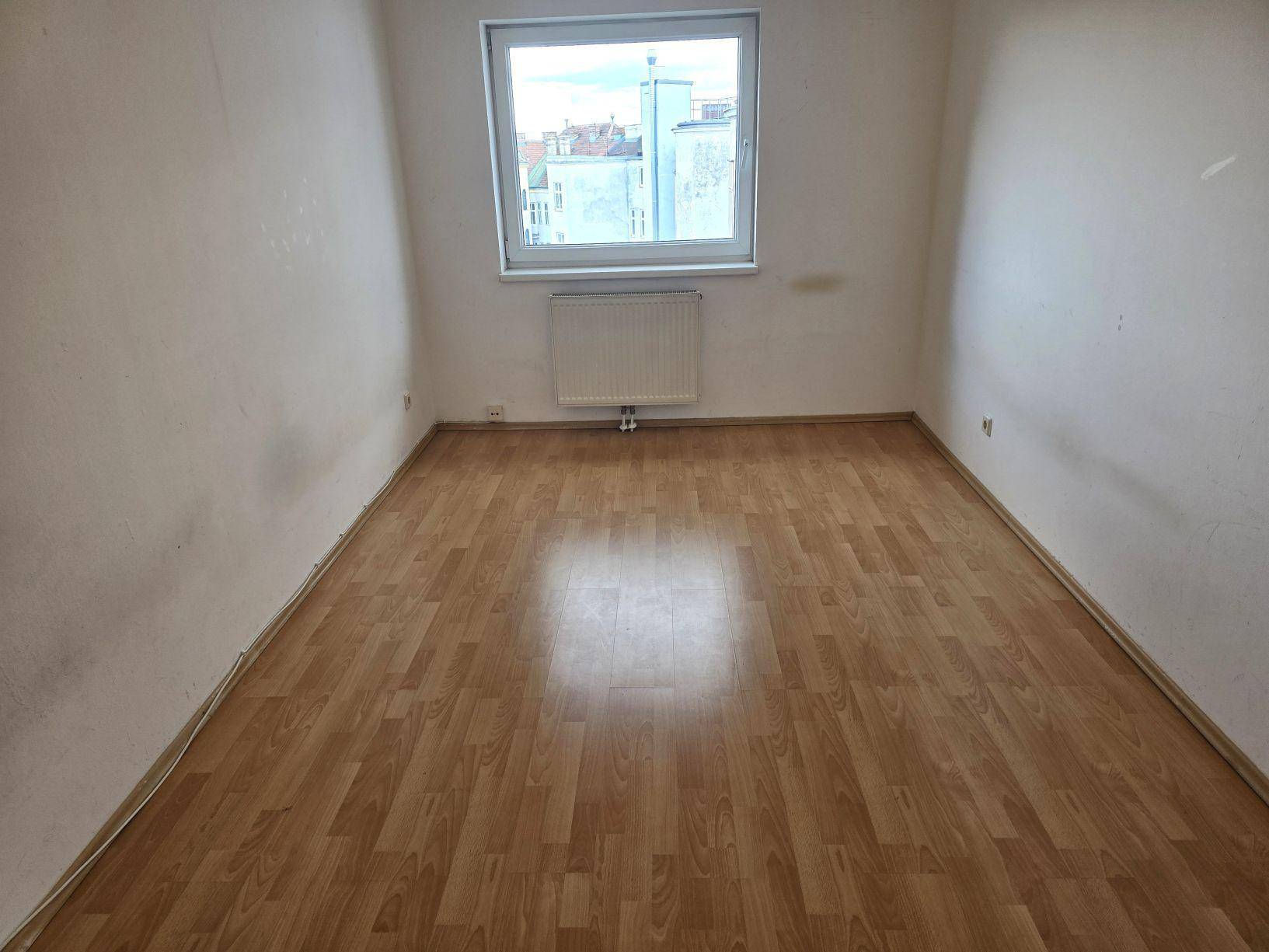 Helles Schlafzimmer mit Laminatboden, weiß gestrichenen Wänden und einem Fenster mit Stadtblick.