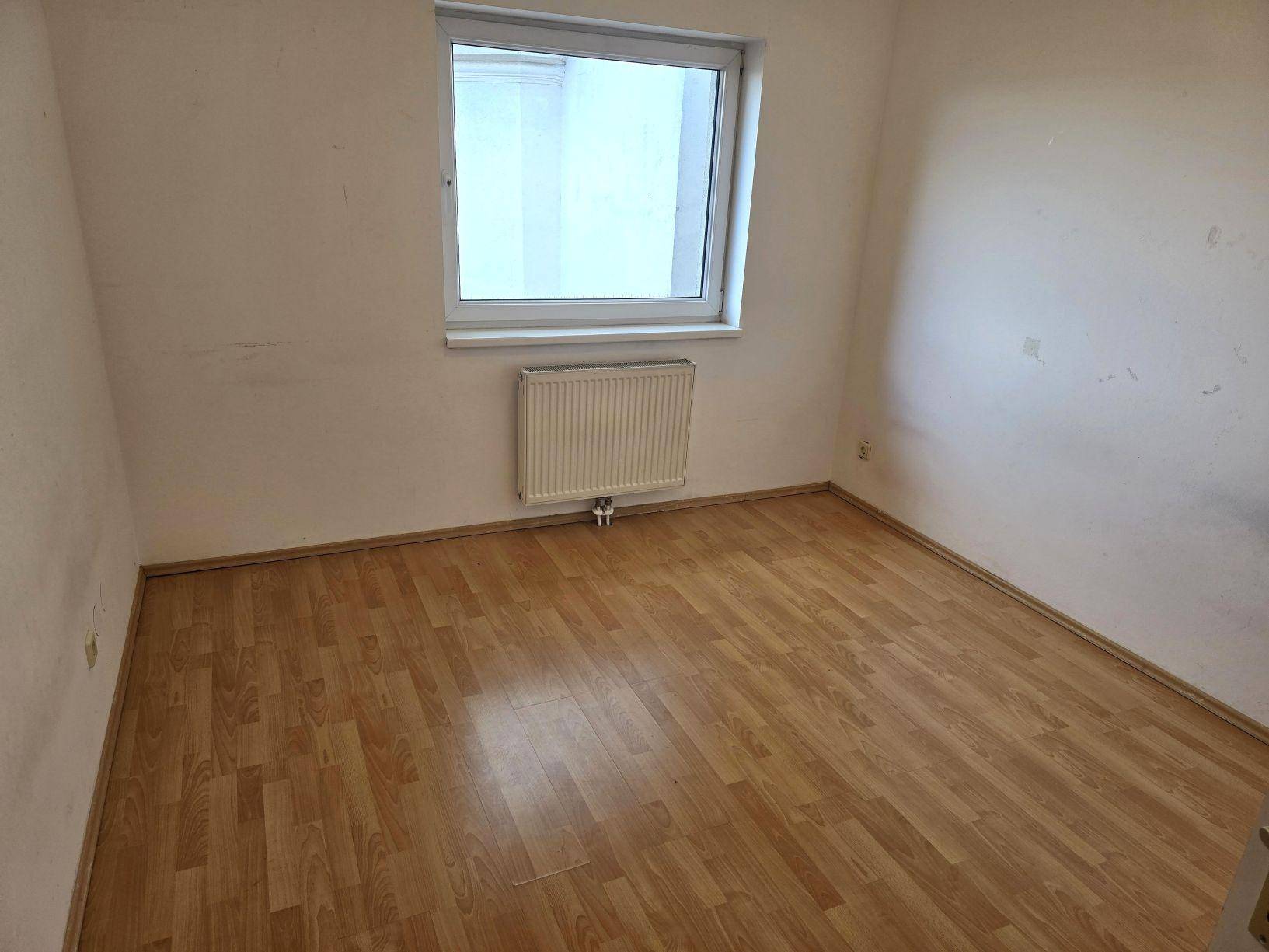 Freundliches Zimmer mit Laminatboden, weiß gestrichenen Wänden und einem Fenster für natürliches Licht.