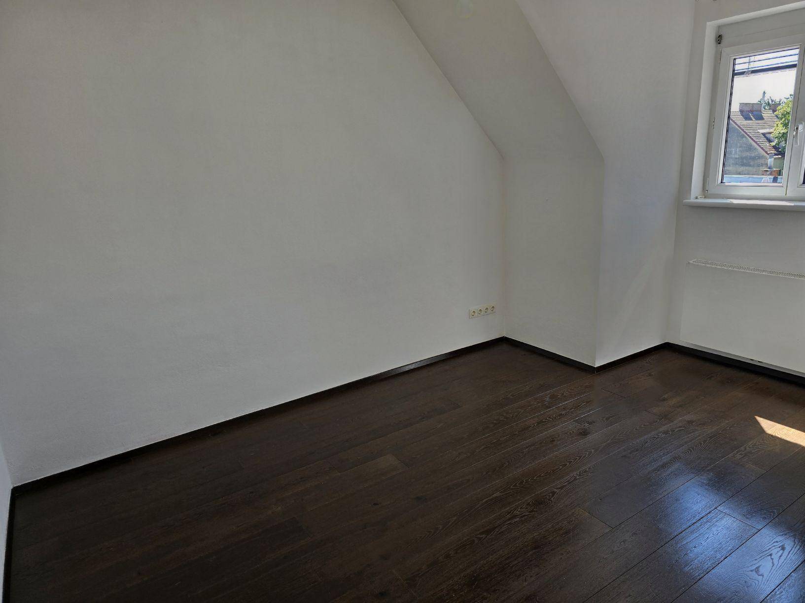 Helles Schlafzimmer mit dunklem Holzboden und großem Fenster, bereit zur Einrichtung.