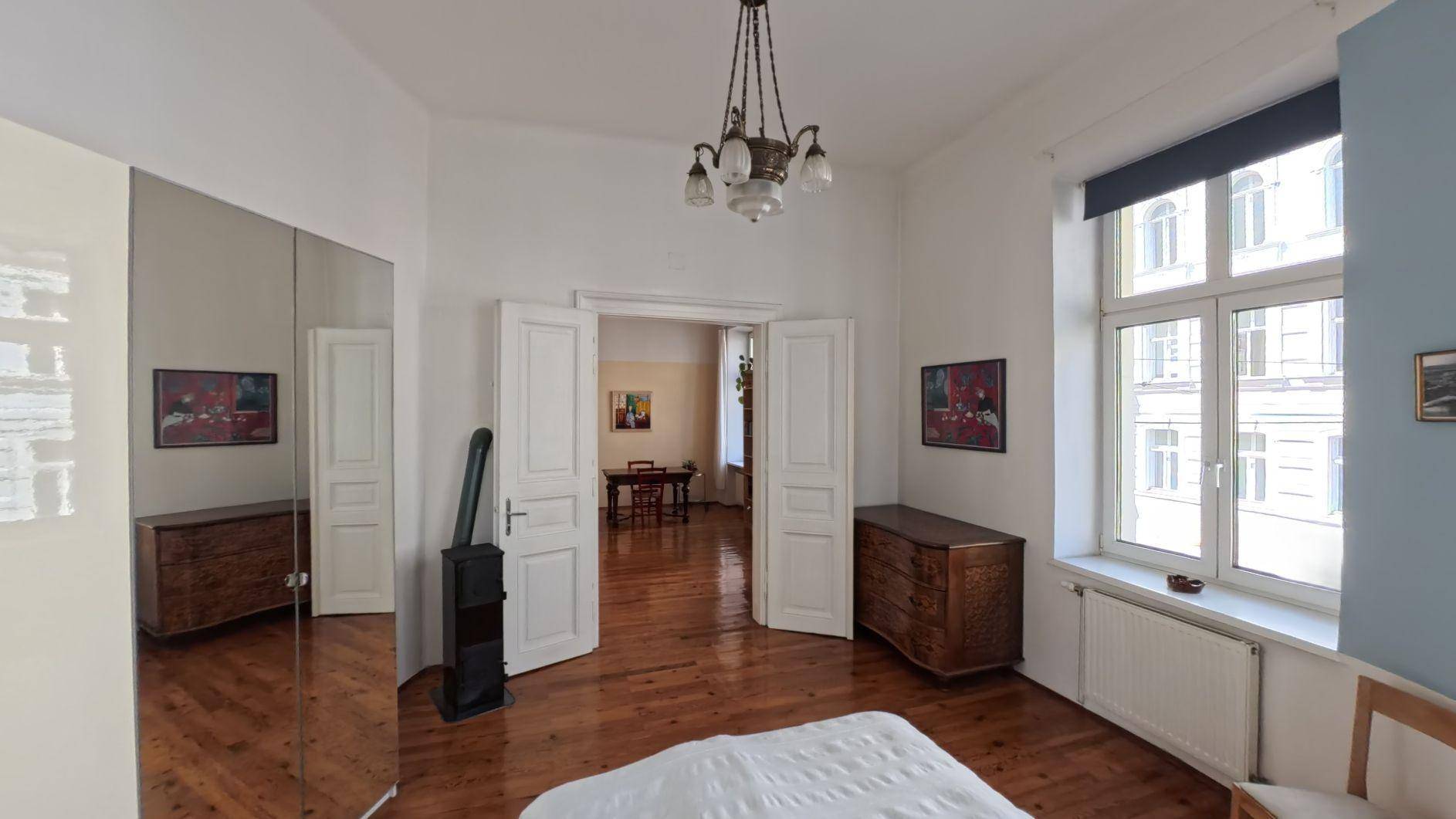 Schlafzimmer mit Holzboden, Spiegelschränken und einem Kaminofen, offen zum Wohnbereich.