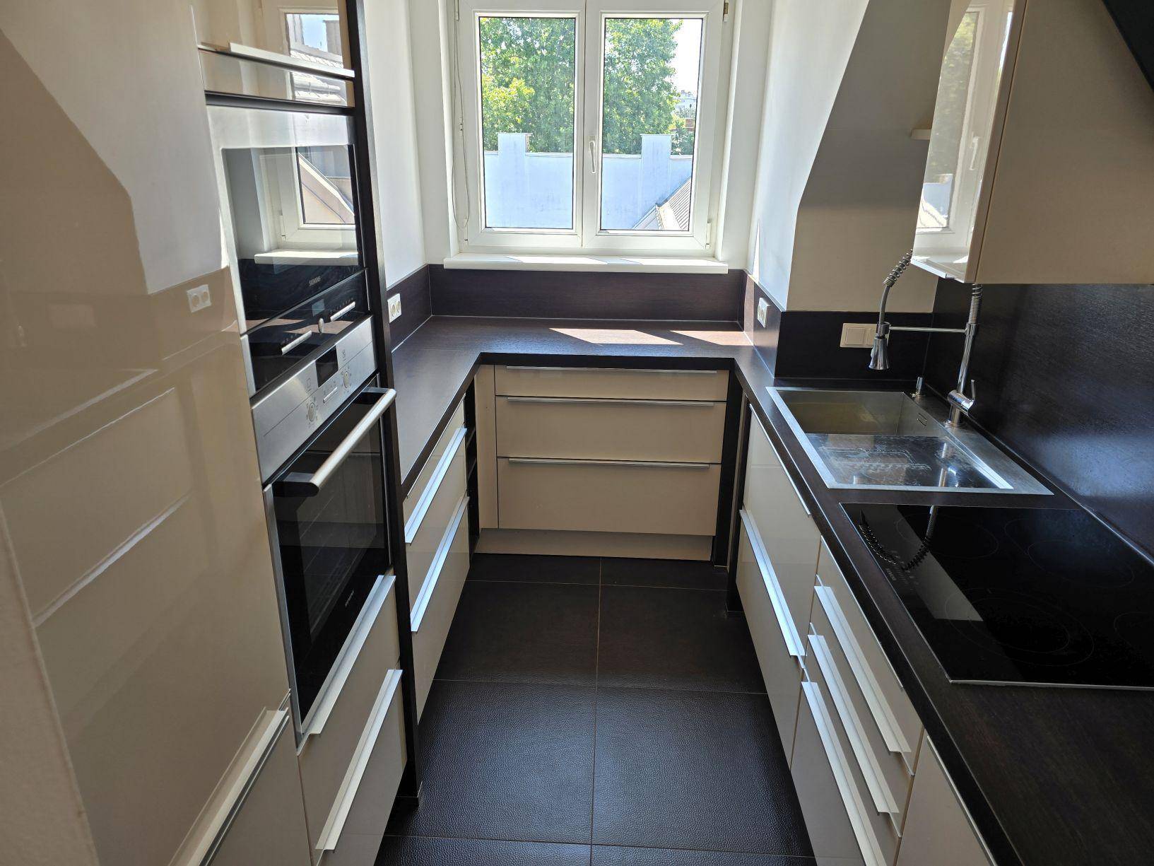 Moderne Küche mit beigen Hochglanzfronten, Einbaugeräten und Fenster für Tageslicht.