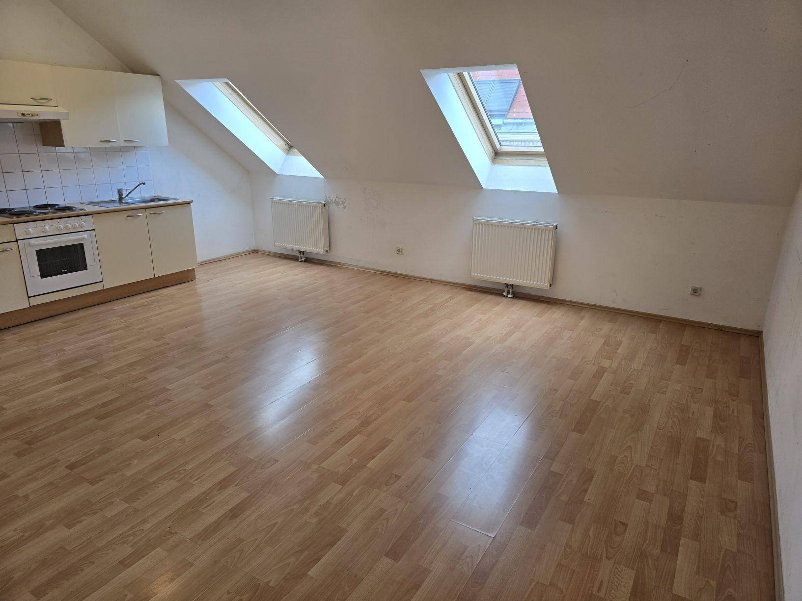 Geräumiger Wohnbereich im Dachgeschoss mit integrierter Küchenzeile und viel Tageslicht durch Dachfenster.