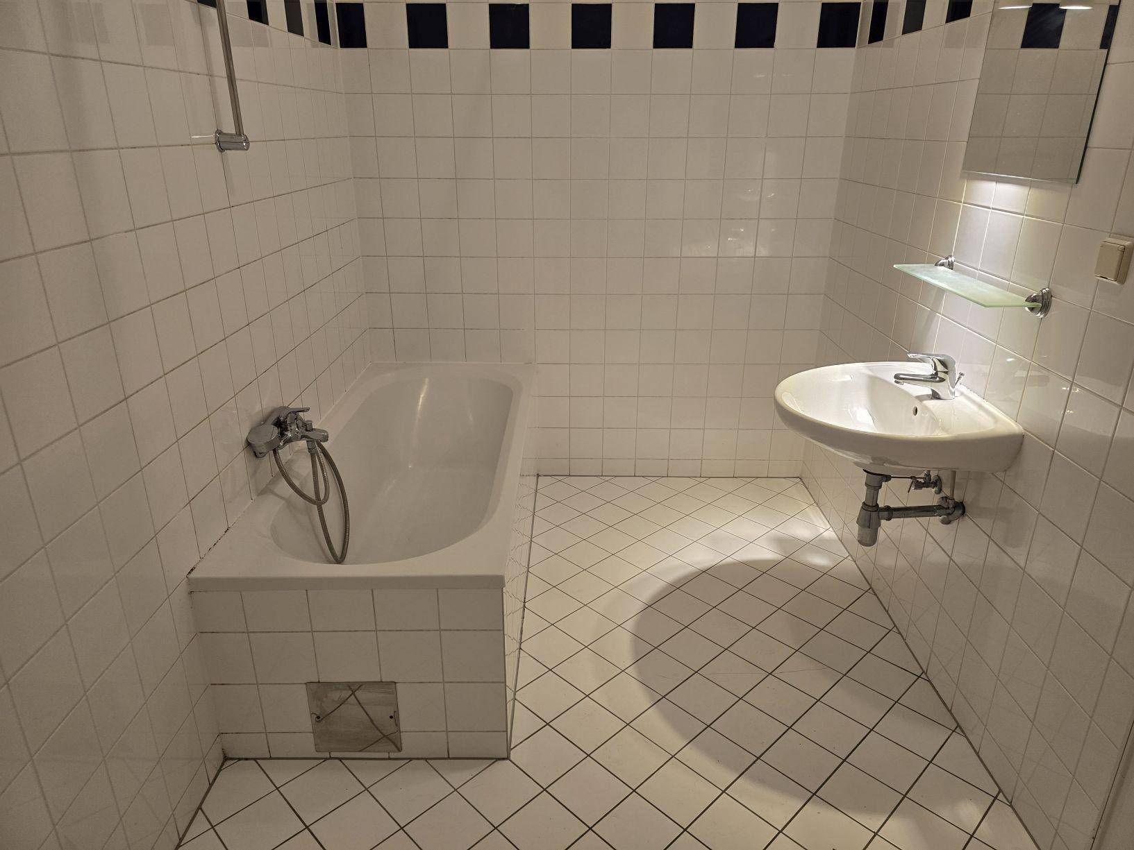 Badezimmer mit weißen Fliesen, Badewanne und Waschbecken mit Spiegel, akzentuiert durch einen blauen Streifen.