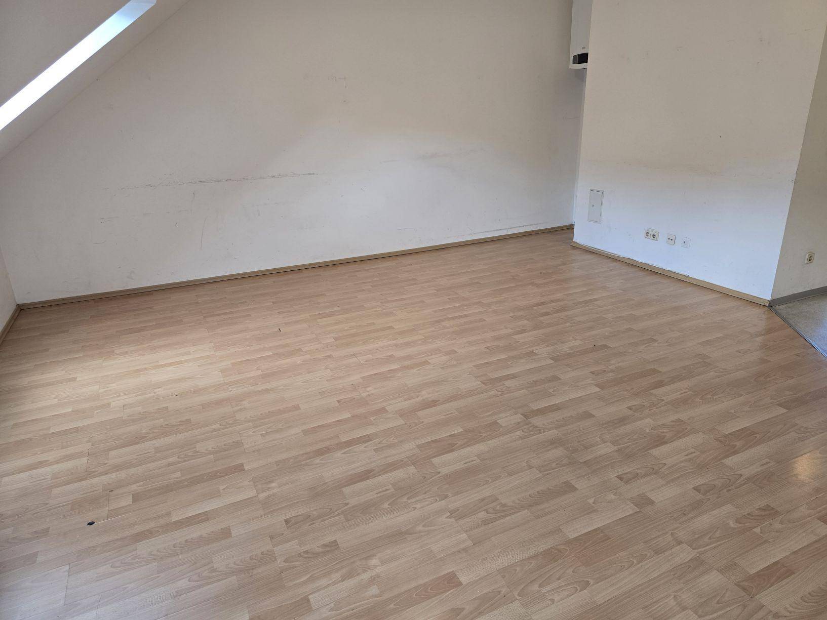 Leerer Raum mit Laminatboden und weißen Wänden, bereit zur individuellen Gestaltung.