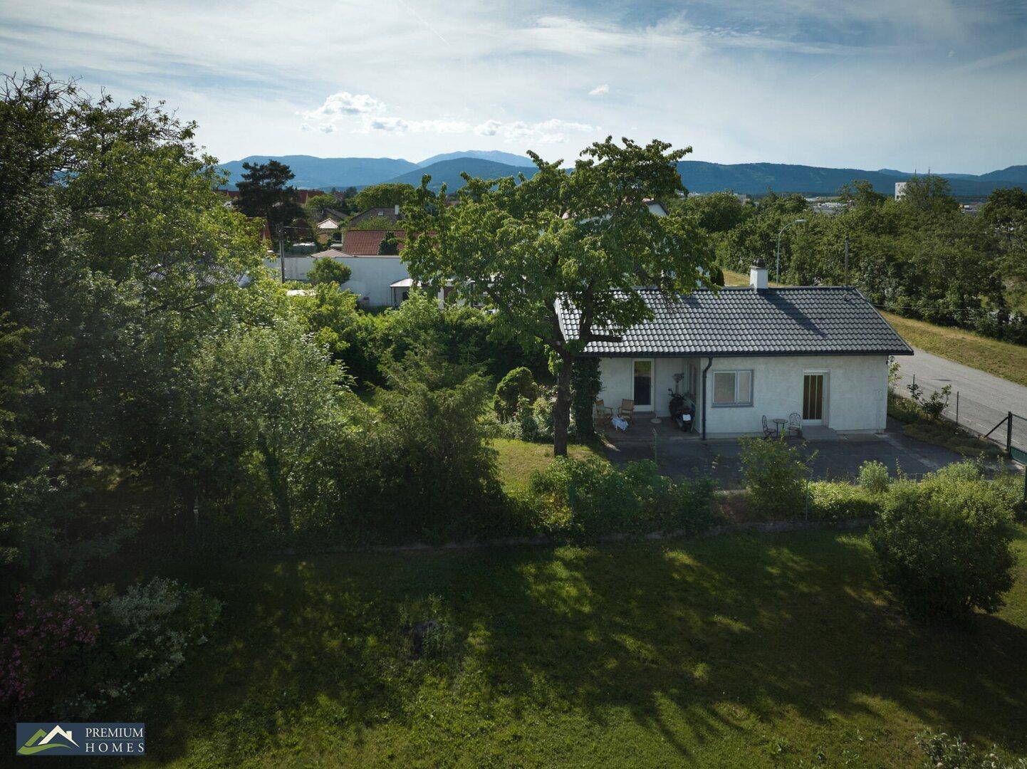 Weitläufiger Gartenbereich mit altem Baumbestand und dem Einfamilienhaus im Hintergrund, mit Bergblick.
