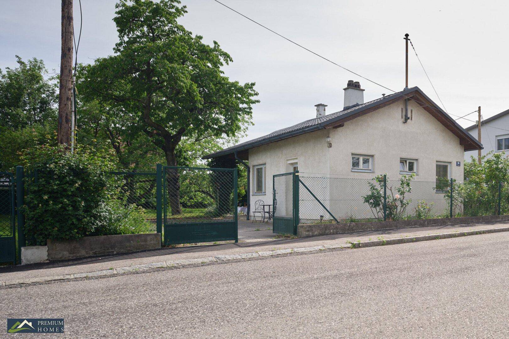 Das Einfamilienhaus von der Straße aus gesehen, mit einem grünen Zaun und Bäumen im Garten.