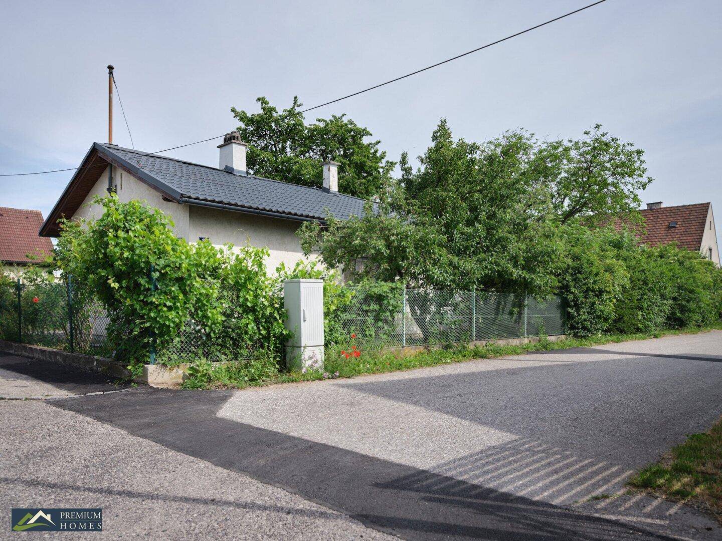 Das Haus an einer Straßenecke, umgeben von Hecken und Bäumen, mit einem gepflegten Garten.
