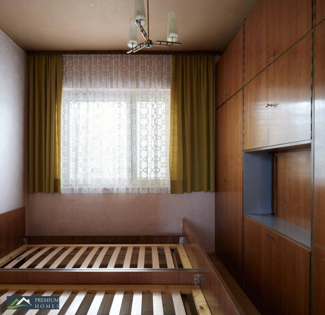 Schlafzimmer mit Einbauschränken, einem Bettgestell und einem Fenster mit Vorhängen.