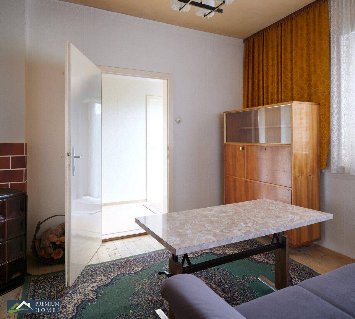 Wohnzimmer mit Couchtisch, Teppich und offenstehender Tür, die den Blick in einen hellen Flur freigibt.
