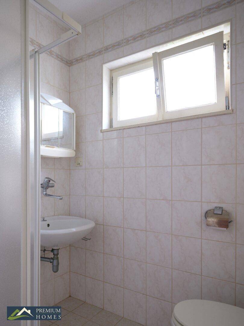 Gefliestes Badezimmer mit Waschbecken, Toilette und einem Fenster für natürliches Licht.