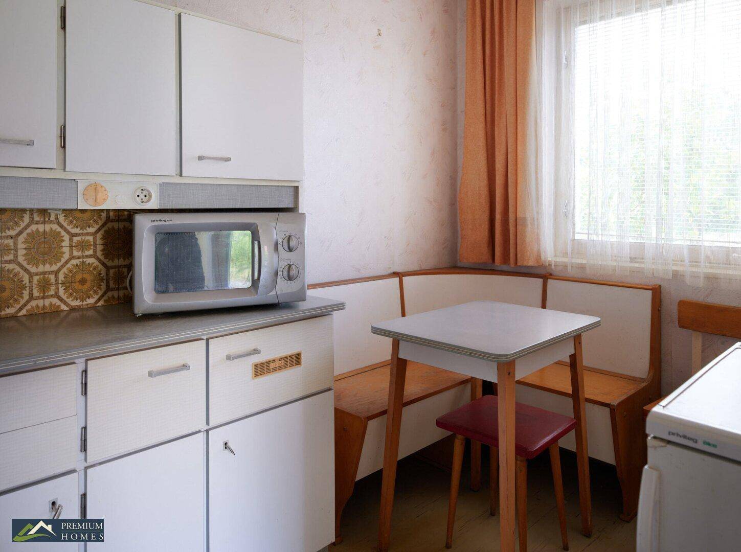 Küche mit weißen Schränken, Mikrowelle und einer gemütlichen Essecke am Fenster.