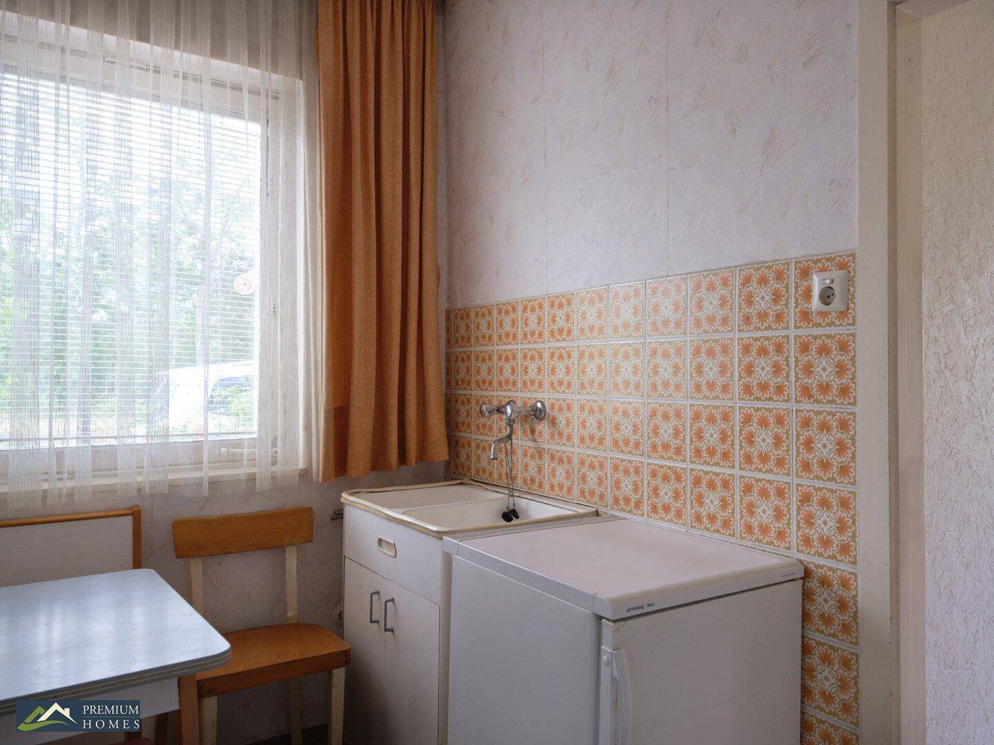 Küche mit Spülbecken, Kühlschrank und einem Fenster, das viel Tageslicht hereinlässt.