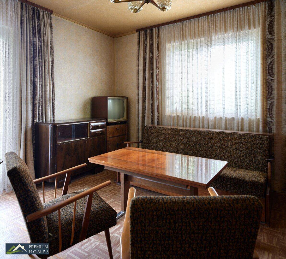 Essbereich mit Holztisch, Stühlen und Sofa, umgeben von Vorhängen und einem Fenster.