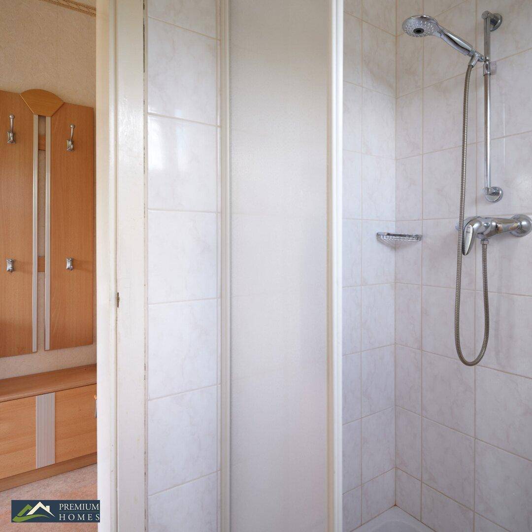 Duschbereich im Badezimmer mit Fliesen und Duschkopf, angrenzend an einen Flur.