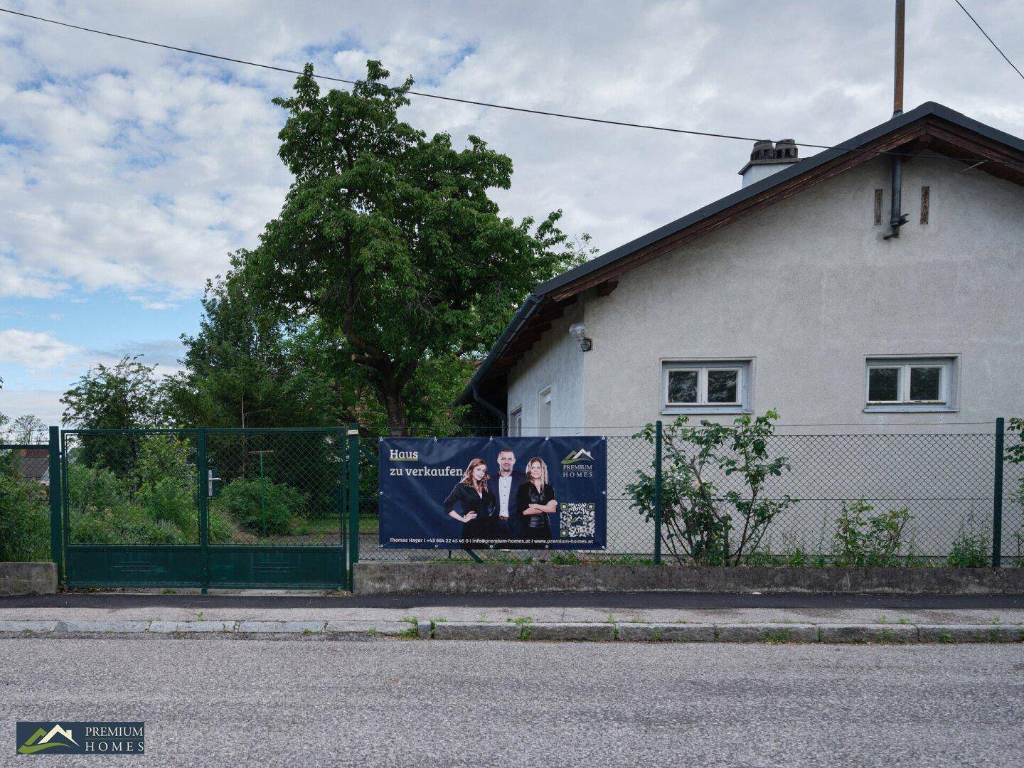 Einfaches Haus mit Garten und einem Verkaufsbanner an der Grundstücksgrenze.