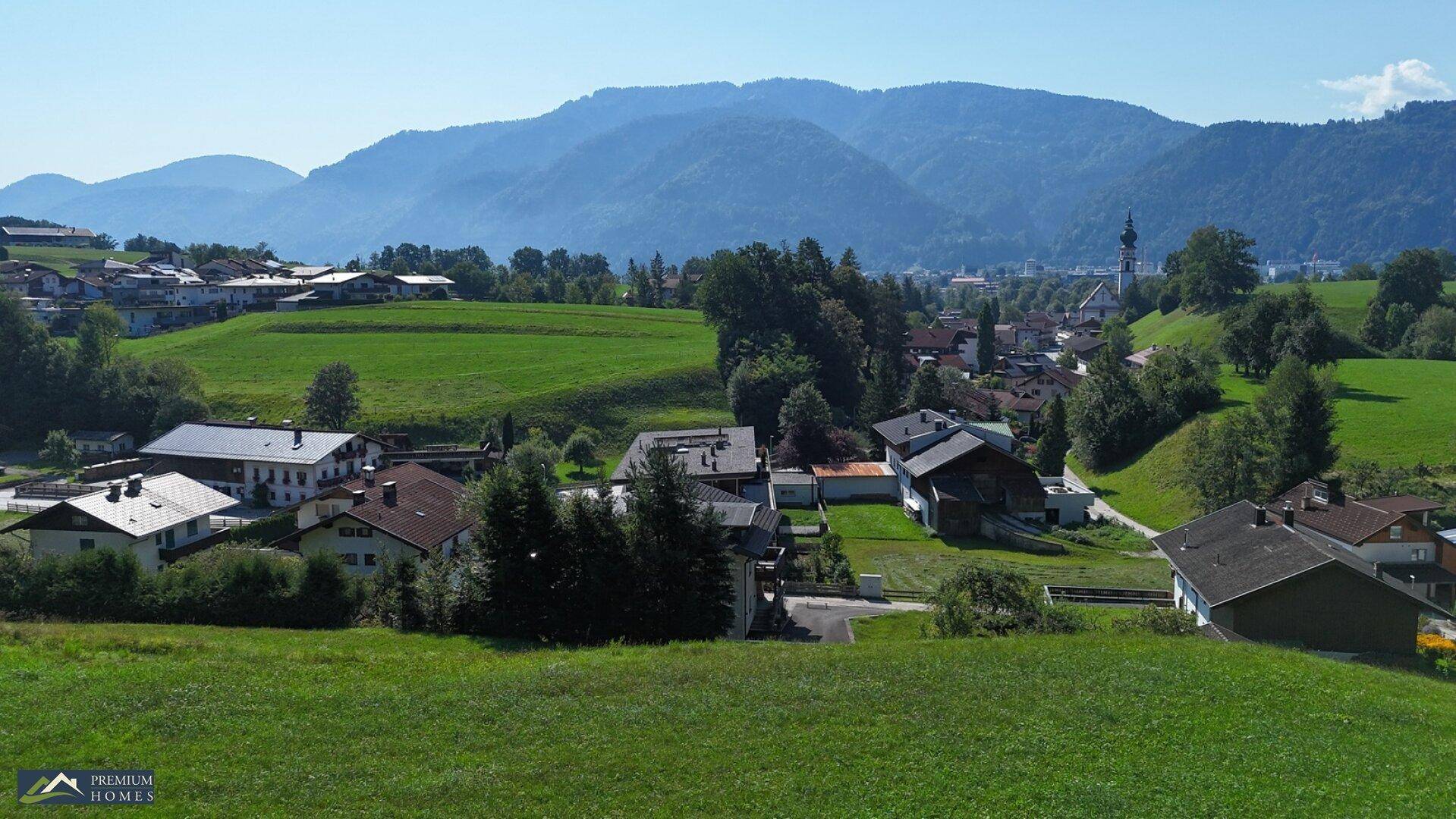 Idyllische Ansicht einer kleinen Ortschaft mit Kirche, umgeben von saftigen Wiesen und majestätischen Bergen.