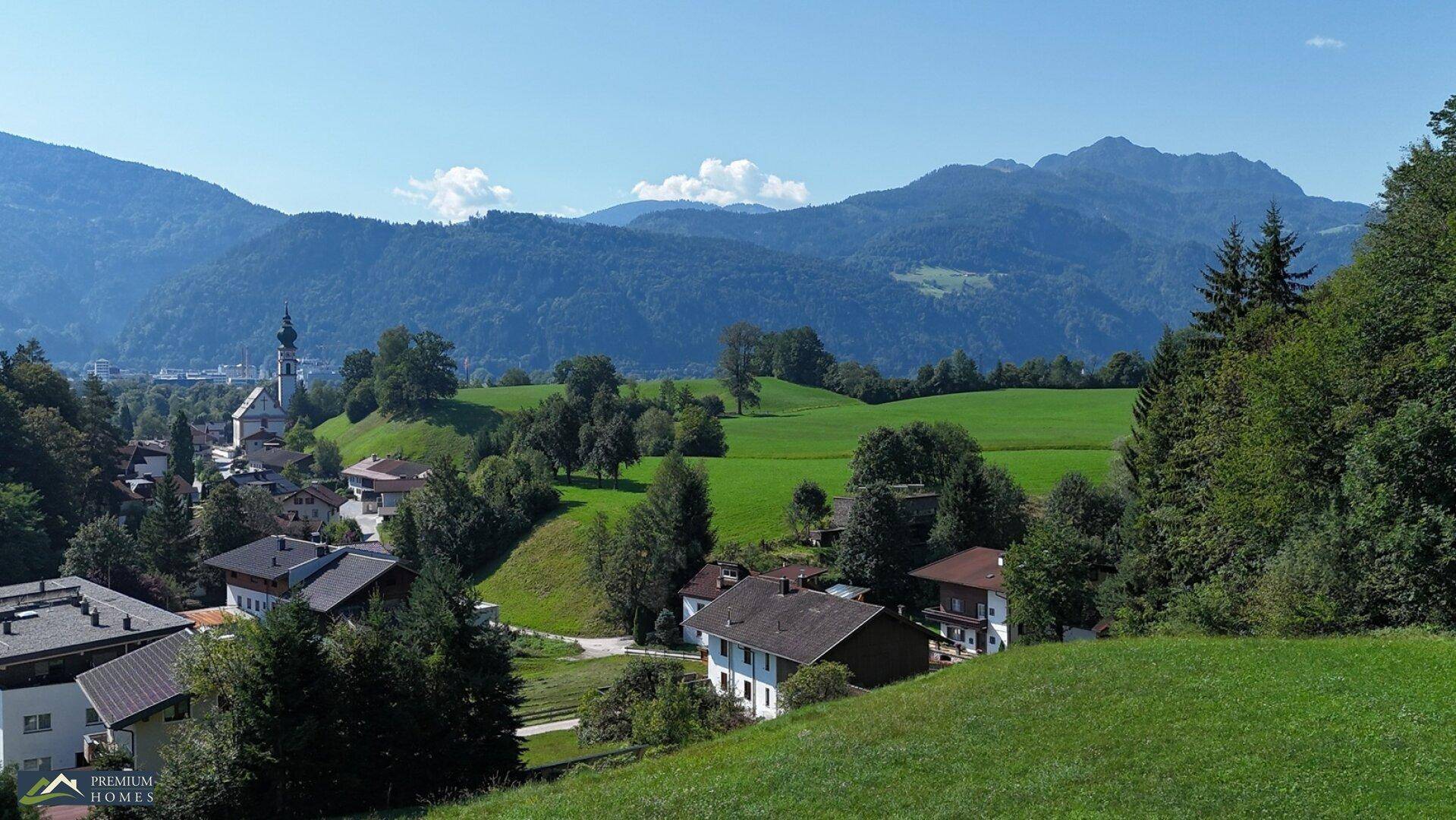 Herrlicher Blick über grüne Wiesen und Dächer auf eine Kirche und die umliegende Bergwelt.