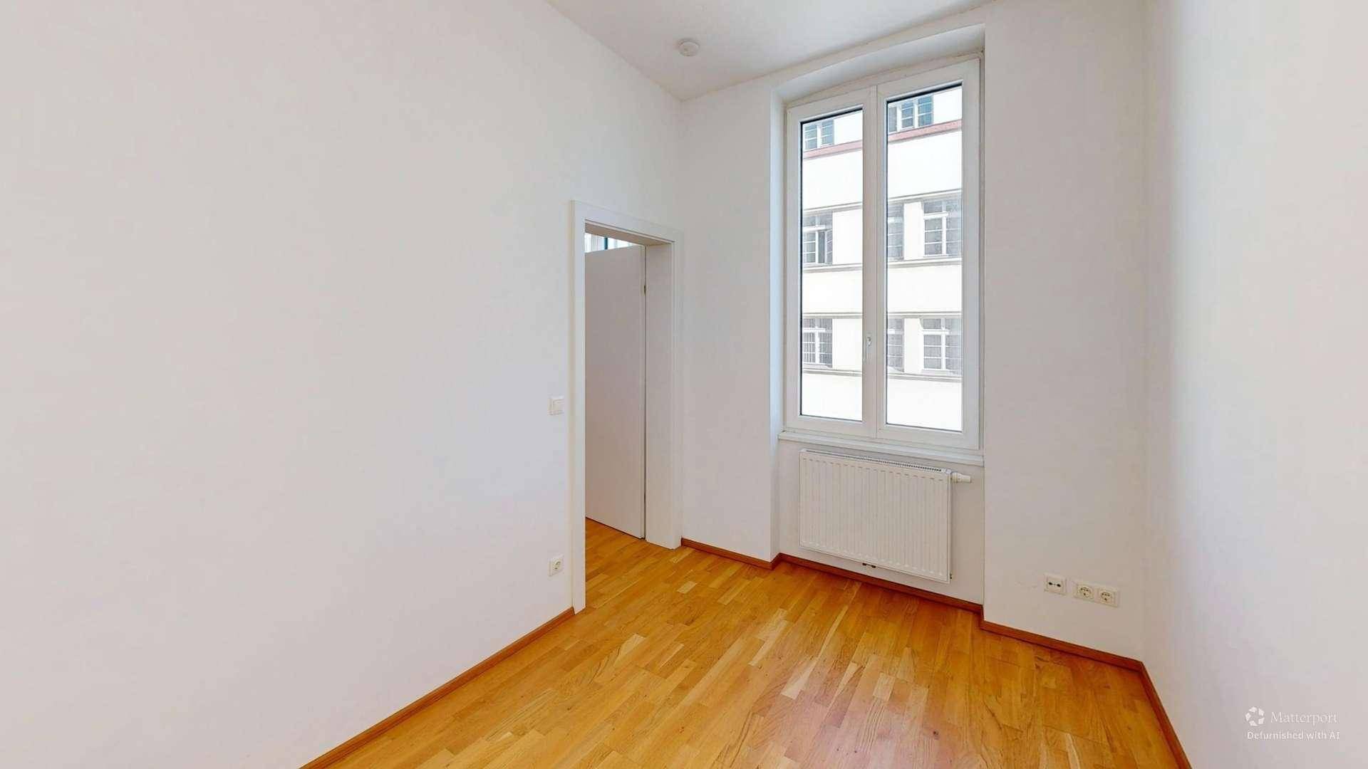 Unmöbliertes Zimmer mit Holzboden und großem Fenster, ideal für Schlafzimmer oder Büro.