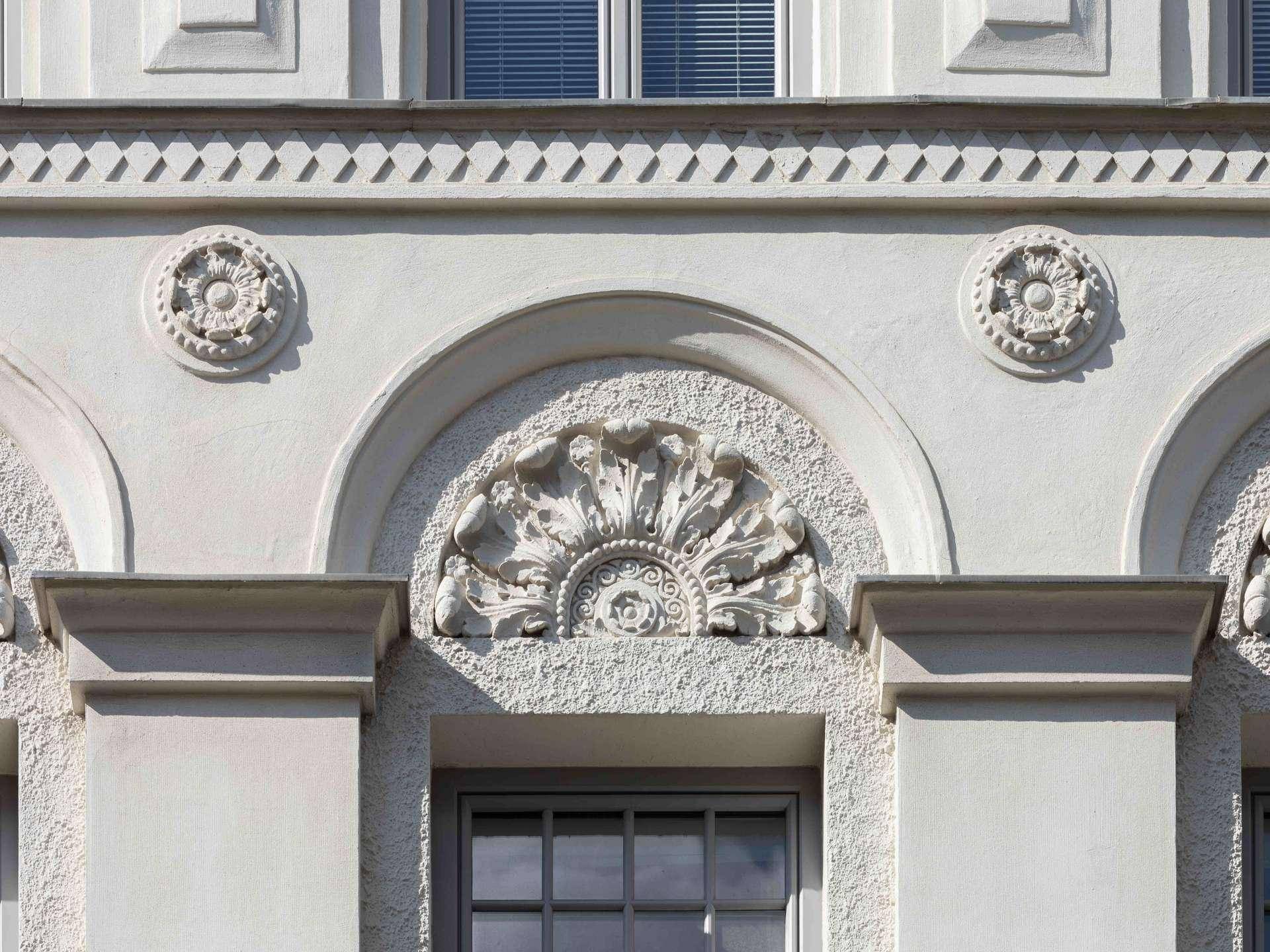 Nahaufnahme der kunstvollen Stuckverzierungen und architektonischen Details an der Fassade.