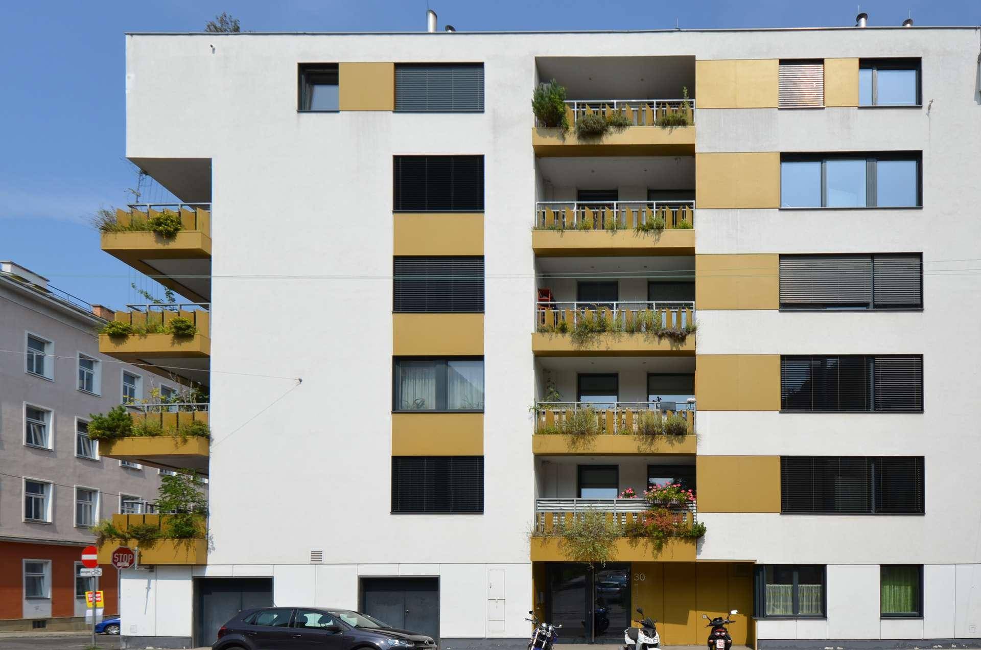 Moderne Fassade eines Wohngebäudes mit weißen und gelben Akzenten sowie Balkonen.
