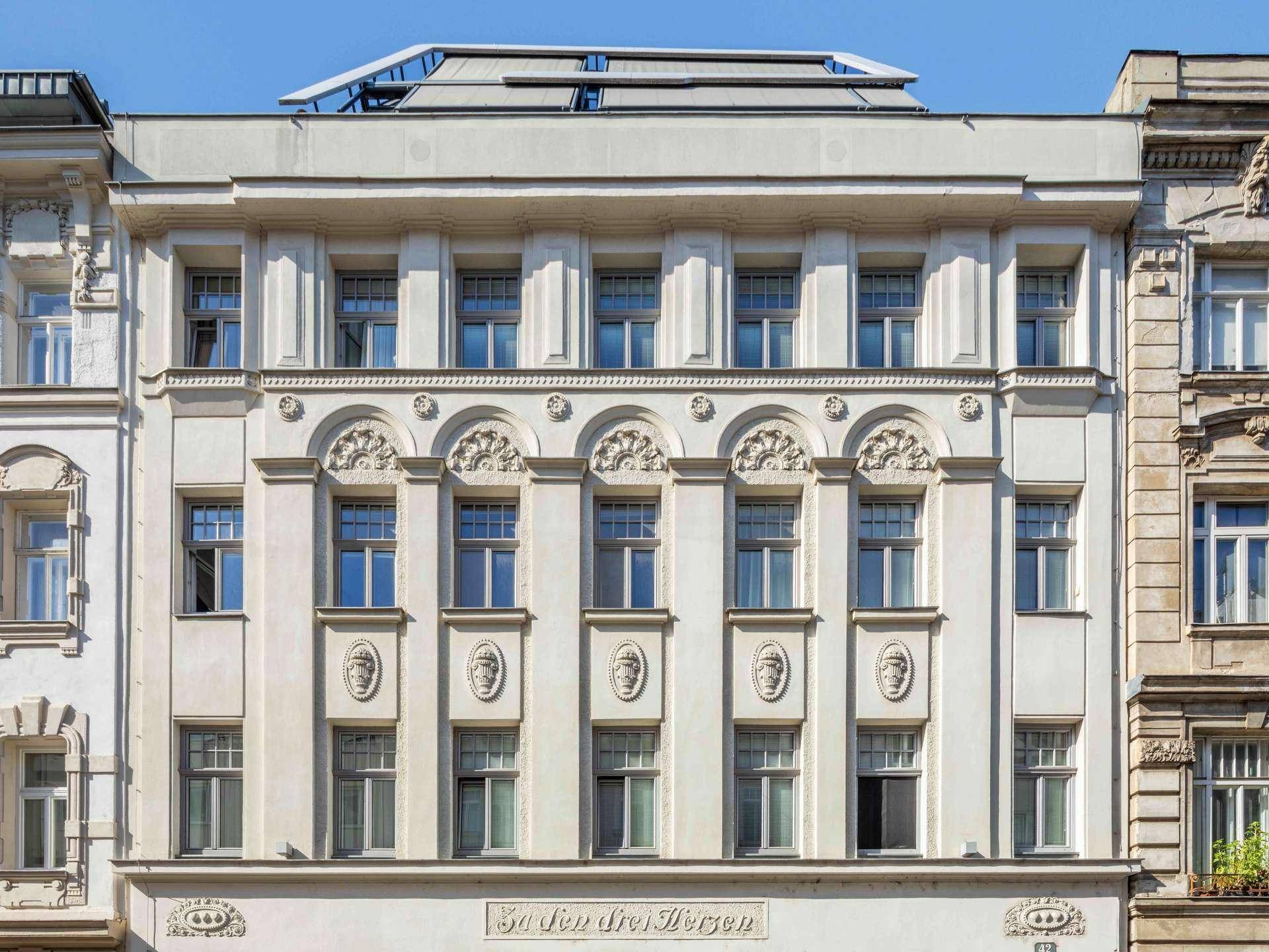 Historische Fassade eines Gebäudes mit reich verzierten Details und modernen Dachaufbauten.