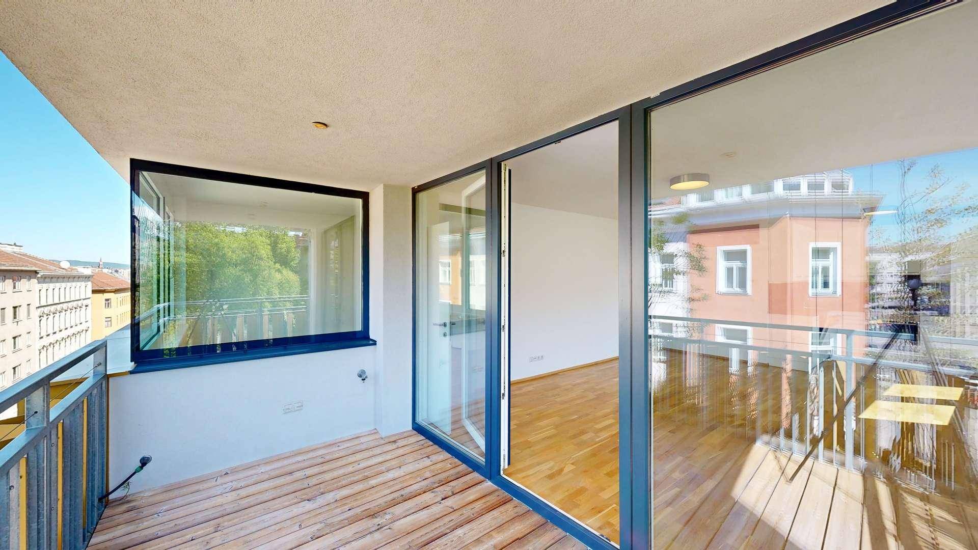 Geräumiger Balkon mit Holzboden und Blick auf die umliegenden Gebäude und Bäume.