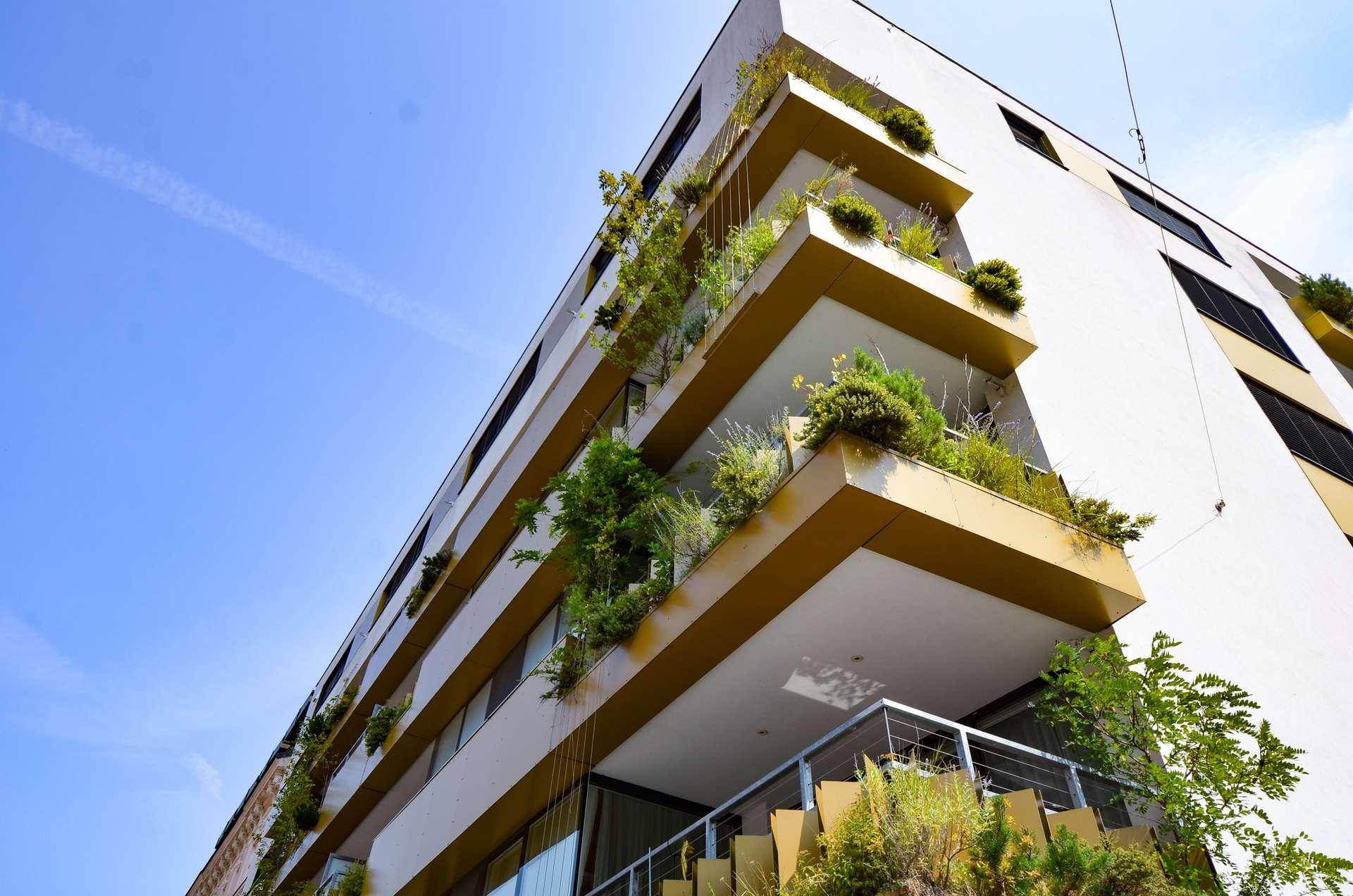 Architektonische Ansicht eines modernen Gebäudes mit begrünten Balkonen unter blauem Himmel.