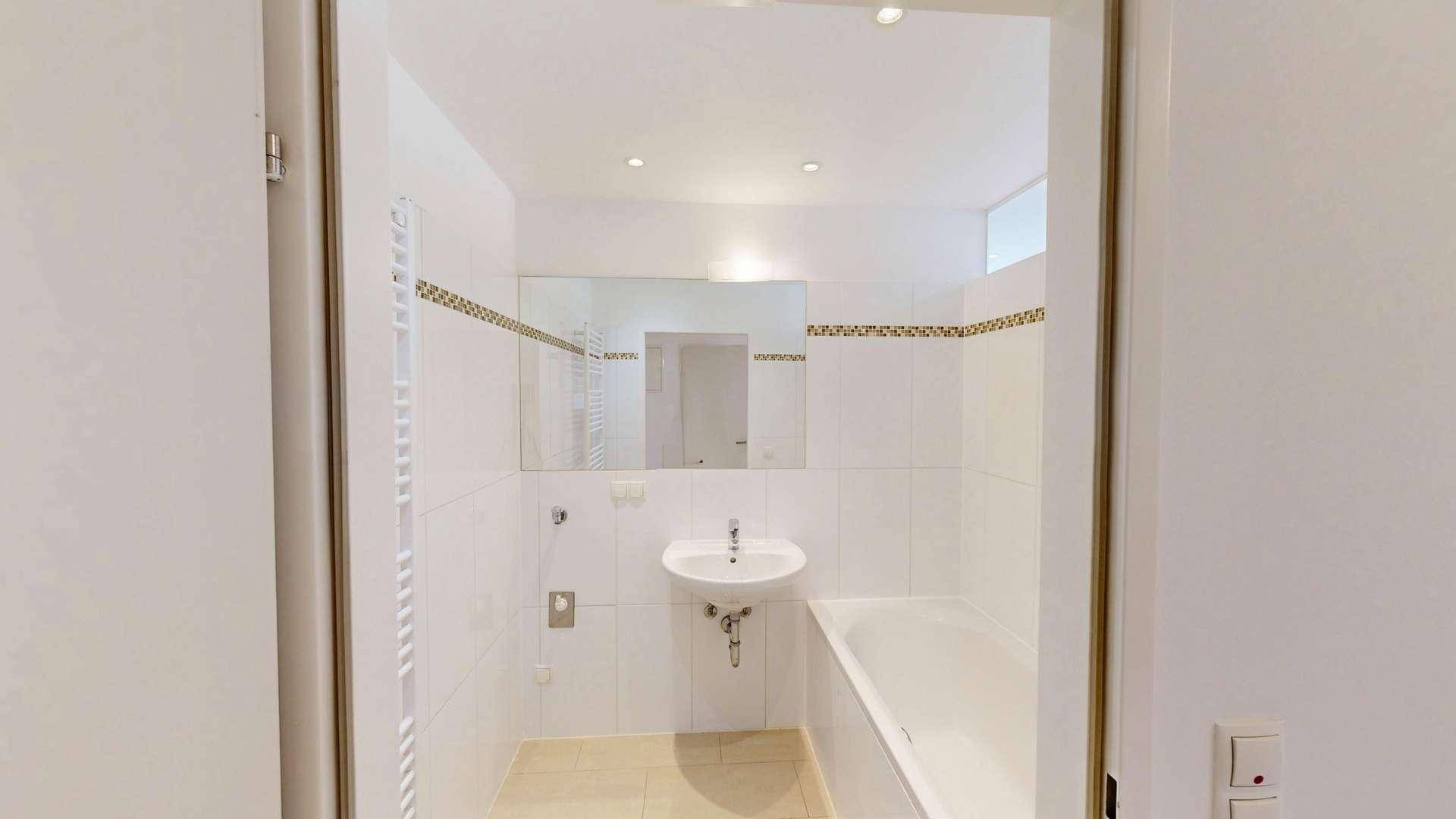 Modernes Badezimmer mit weißen Fliesen, Badewanne, Waschbecken und Handtuchheizkörper.