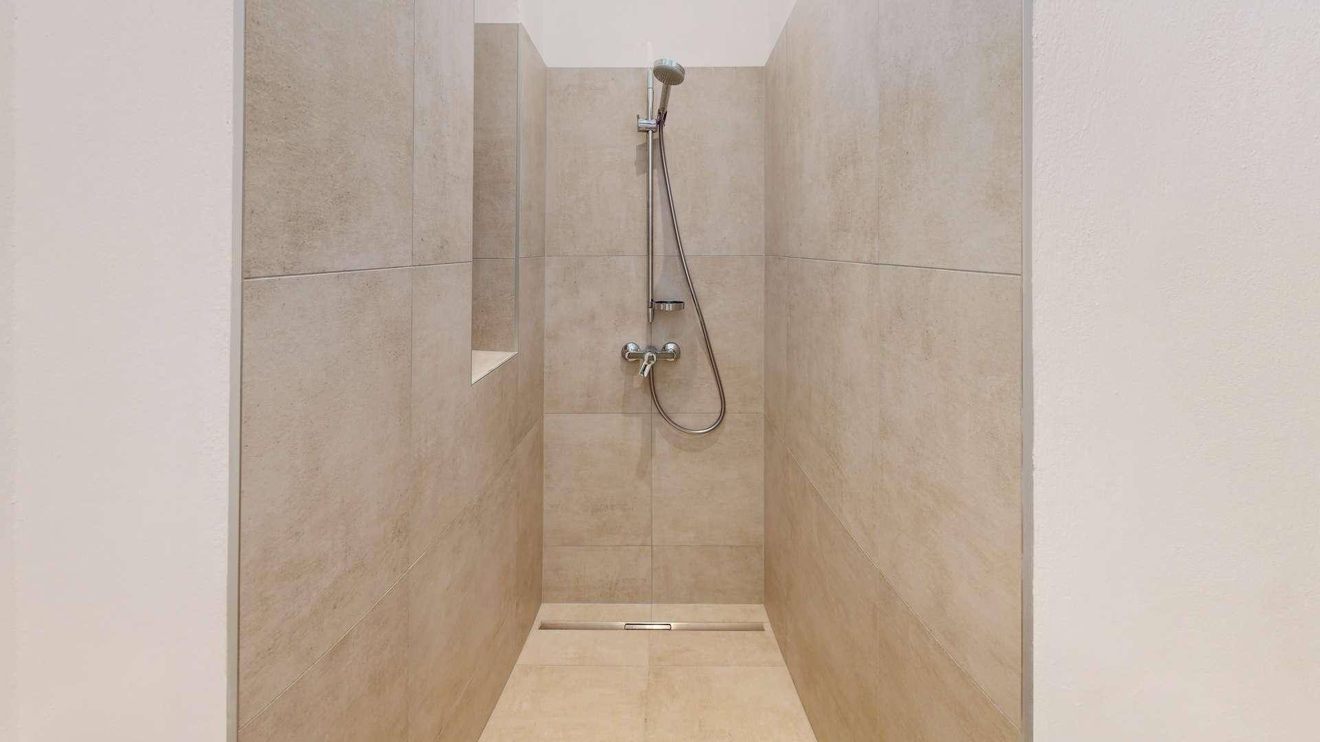 Geräumige, begehbare Dusche mit beigefarbenen Fliesen und minimalistischem Duschkopf.