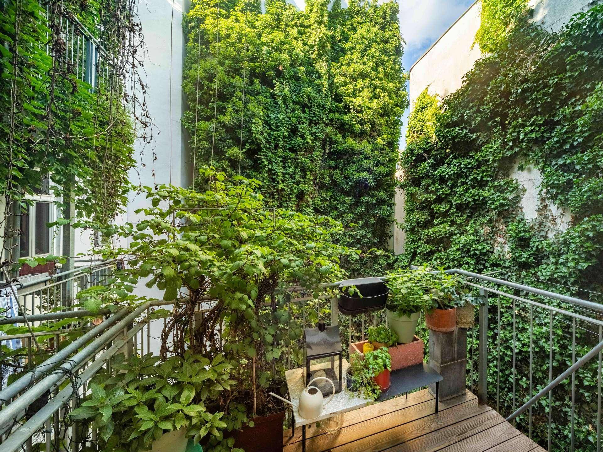 Kleiner, gemütlicher Balkon mit Holzdeck, Topfpflanzen und Blick auf grüne Wände.