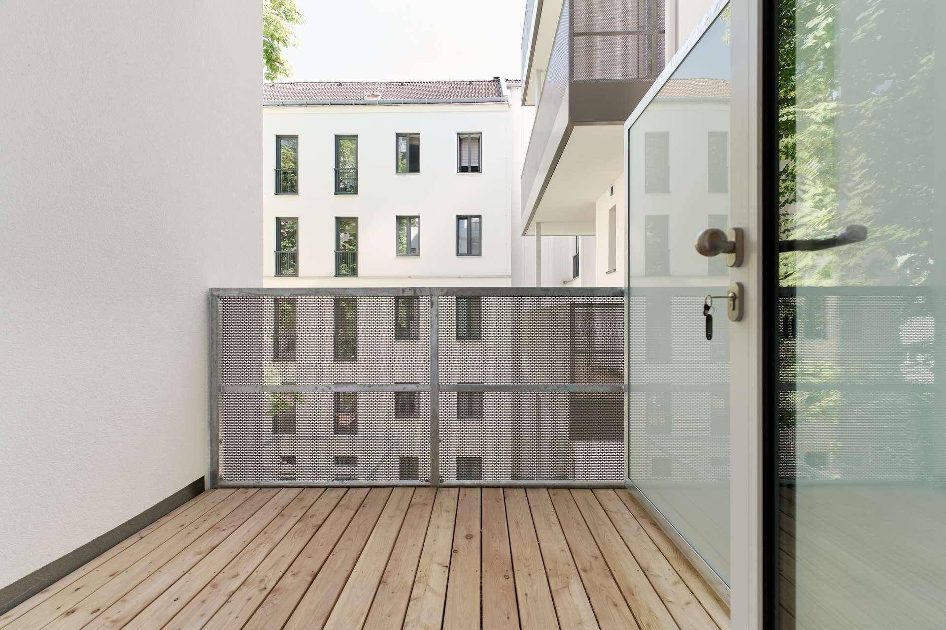 Balkon mit Holzfußboden und Metallgeländer, bietet einen Blick auf die umliegenden Gebäude.