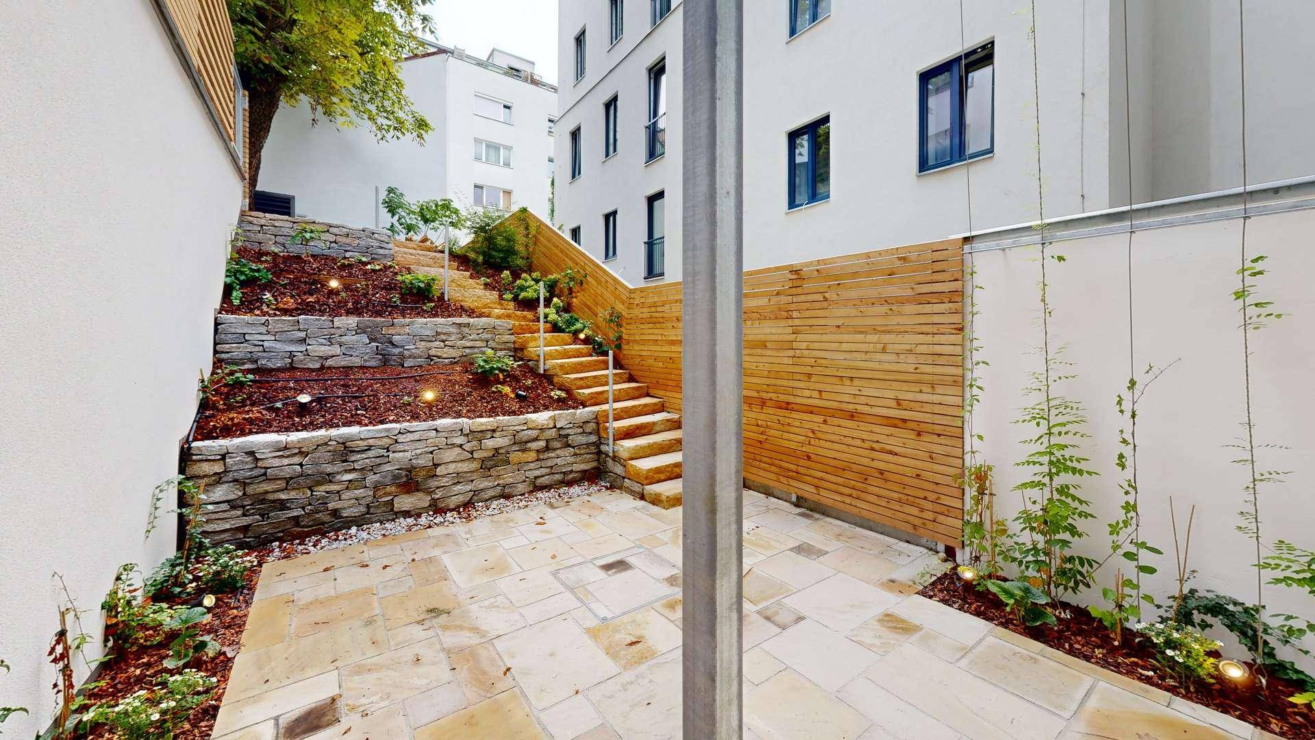 Gestalteter Gartenbereich mit Steinterrassen, Bepflanzung und Holzverkleidung, ideal zum Entspannen.