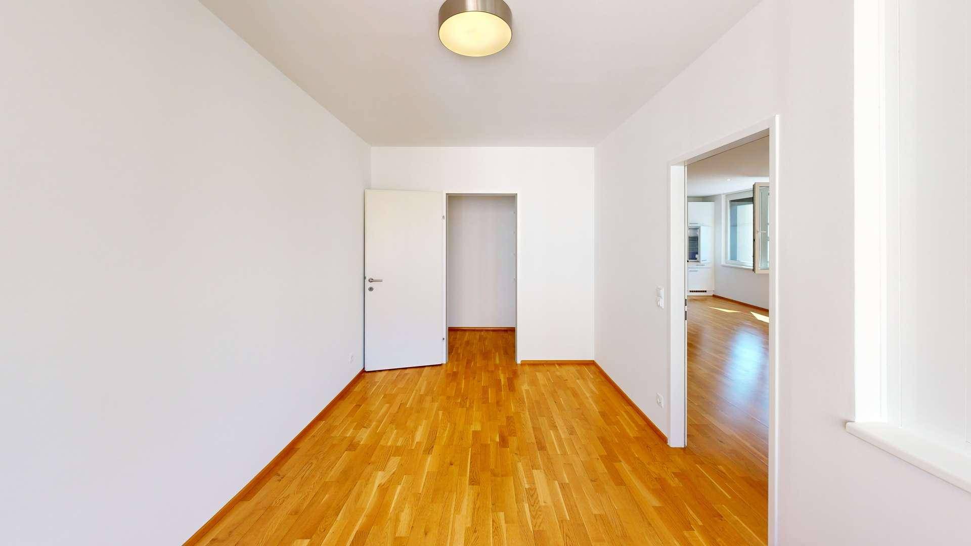 Helles, leeres Zimmer mit Parkettboden und Zugang zu weiteren Räumen.