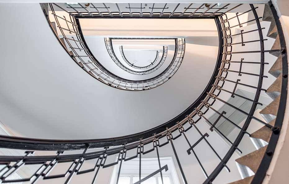 Elegantes Treppenhaus mit schmiedeeisernem Geländer und Blick nach oben, typisch für Altbauten.